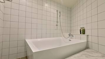 Une salle de bain moderne avec des carreaux blancs, une baignoire sur pieds et une petite étagère contenant des articles de toilette.