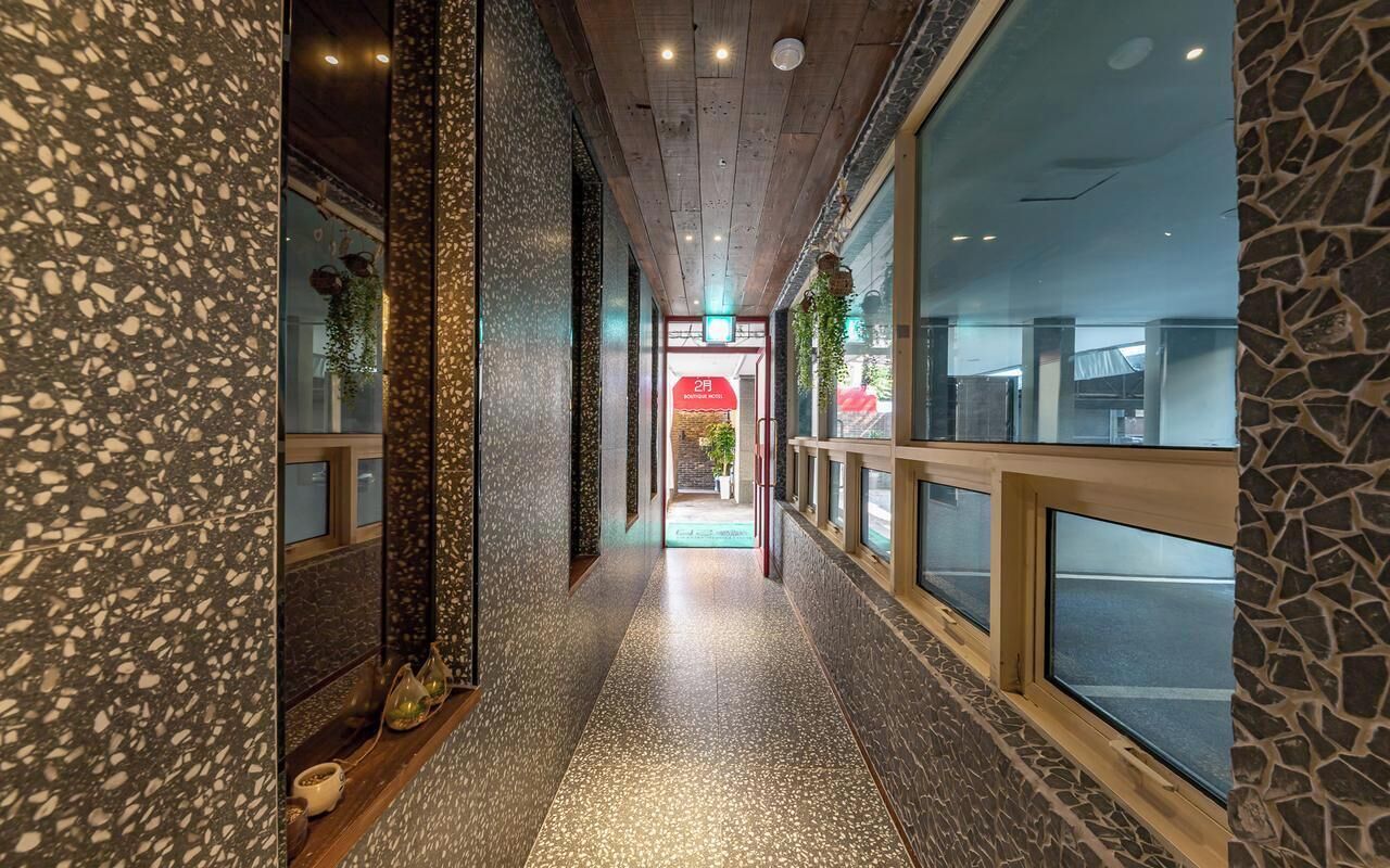 Un pasillo con piso de terrazo, paredes de piedra y ventanas grandes.