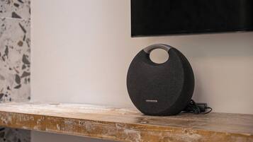 A black speaker with a circular design on a wooden surface, a television mounted on the wall, and a terrazzo floor.