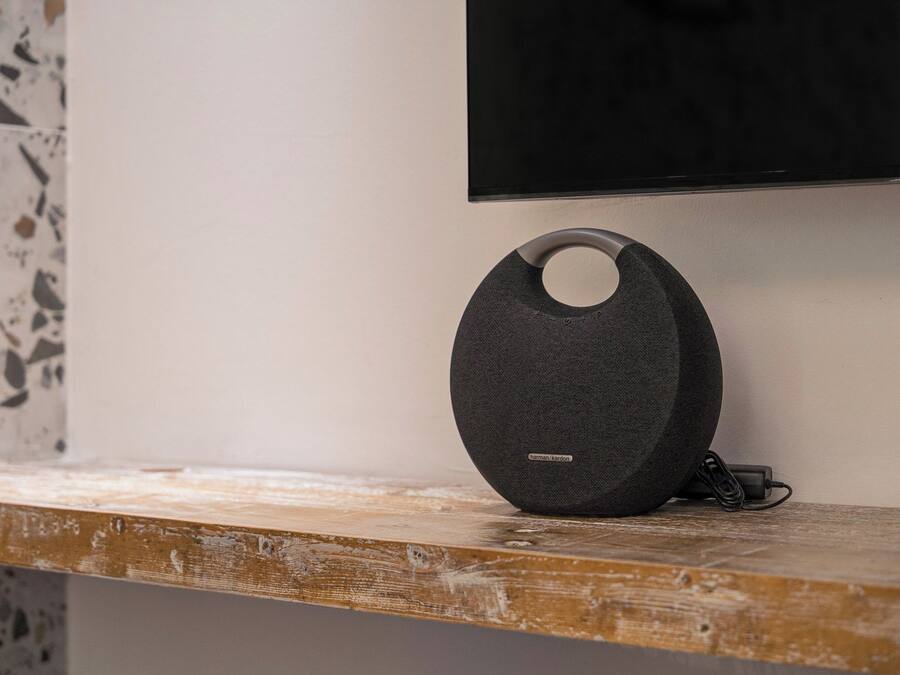 A black speaker with a circular design on a wooden surface, a television mounted on the wall, and a terrazzo floor.