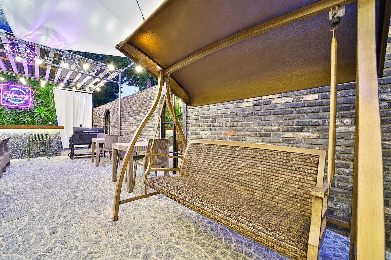 An outdoor seating area with a swing, a grill, and a neon sign.