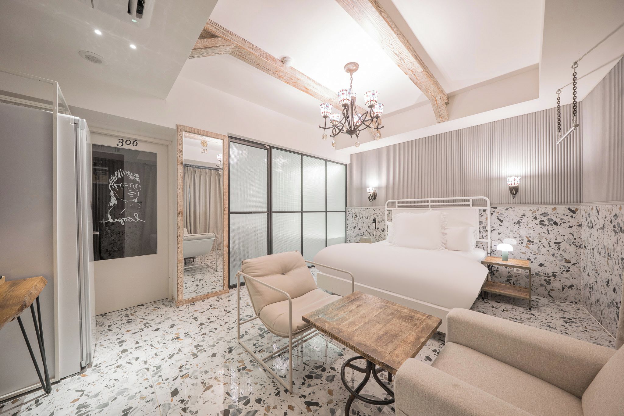 Un dormitorio moderno con una cama grande, una mesa de madera, una silla, una araña y una puerta corrediza de cristal.