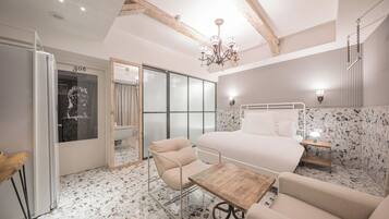 A modern bedroom with a large bed, a wooden table, a chair, a chandelier, and a sliding glass door.