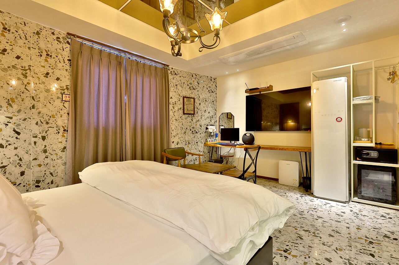 A hotel room with a bed, a desk with a computer, a television, and a minibar.