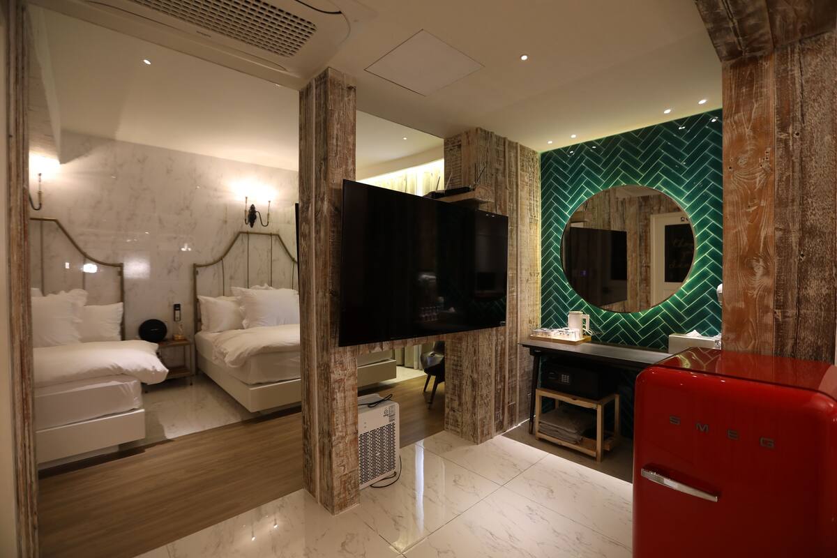 A modern hotel room with a bed, a TV, a mirror, and a red refrigerator.