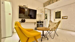 A modern living room with a flat-screen TV, a yellow armchair, a wooden table, and a glass cabinet. - February Hotel Sungseo (Daegu)