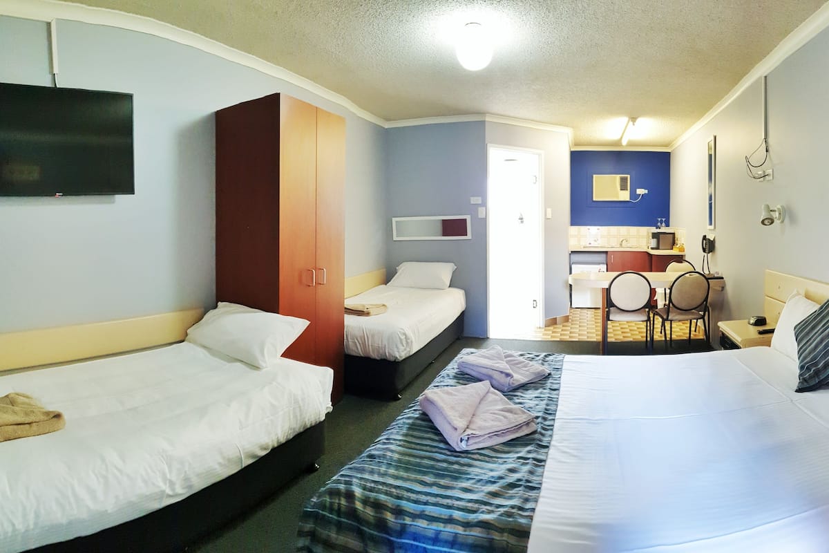 A hotel room with two single beds, a wardrobe, a television, a bathroom with a sink and mirror, and a small dining area.