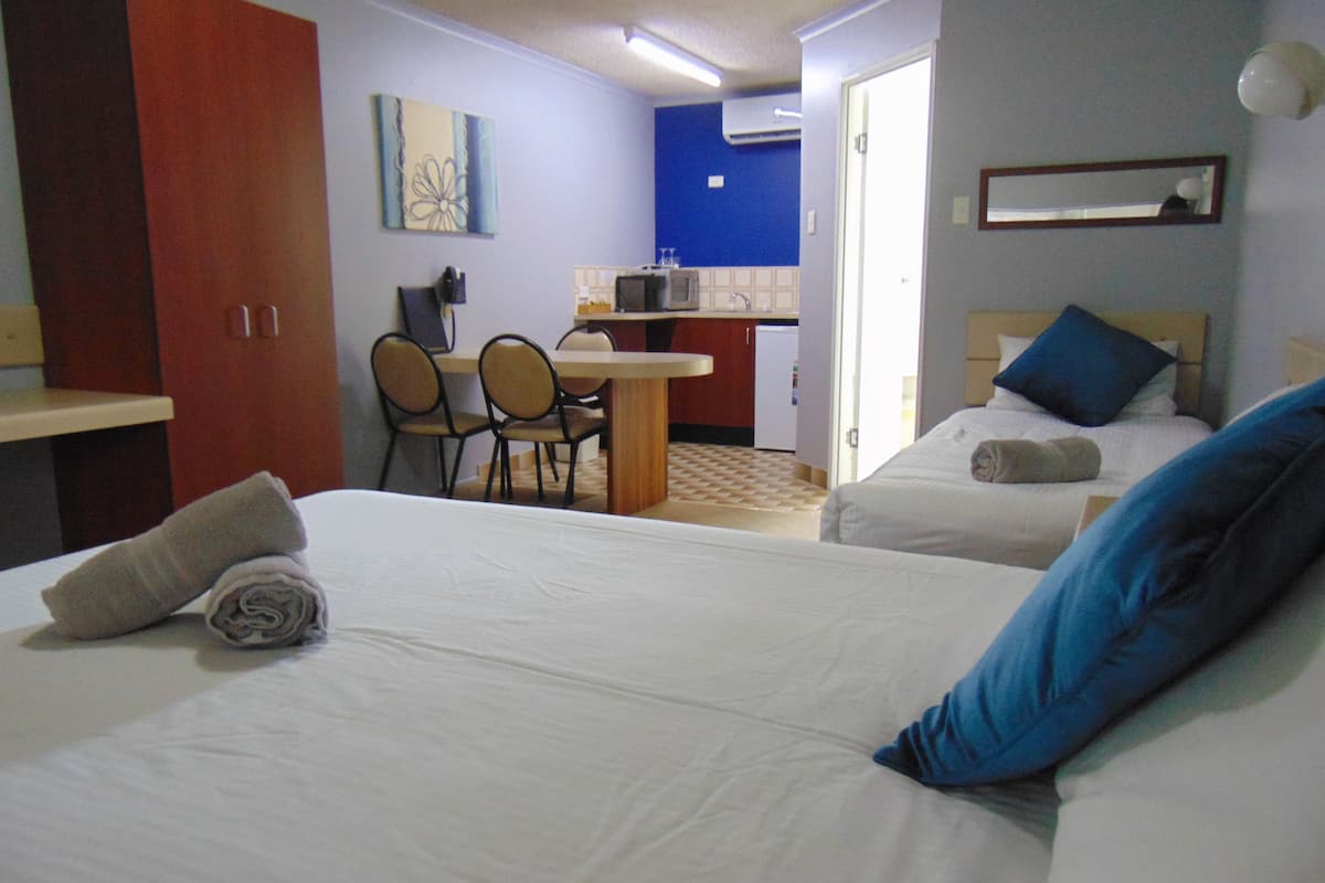A hotel room with two beds, a desk, and a kitchenette.