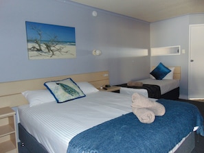 Une chambre d’hôtel avec deux lits, un tableau représentant une plage, une table de chevet et une porte.