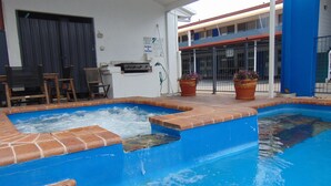 A swimming pool with a brick border and a blue interior. There are two potted plants on the poolside. - Rockhampton Court Motor Inn (Rockhampton)
