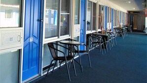 A row of blue doors with windows, each marked with a number. There are tables and chairs arranged in the room. - Rockhampton Court Motor Inn (Rockhampton)