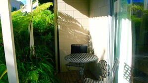 A small outdoor patio with a round metal table and two chairs, surrounded by lush green plants. - Sea Vista Apartments (Auckland)