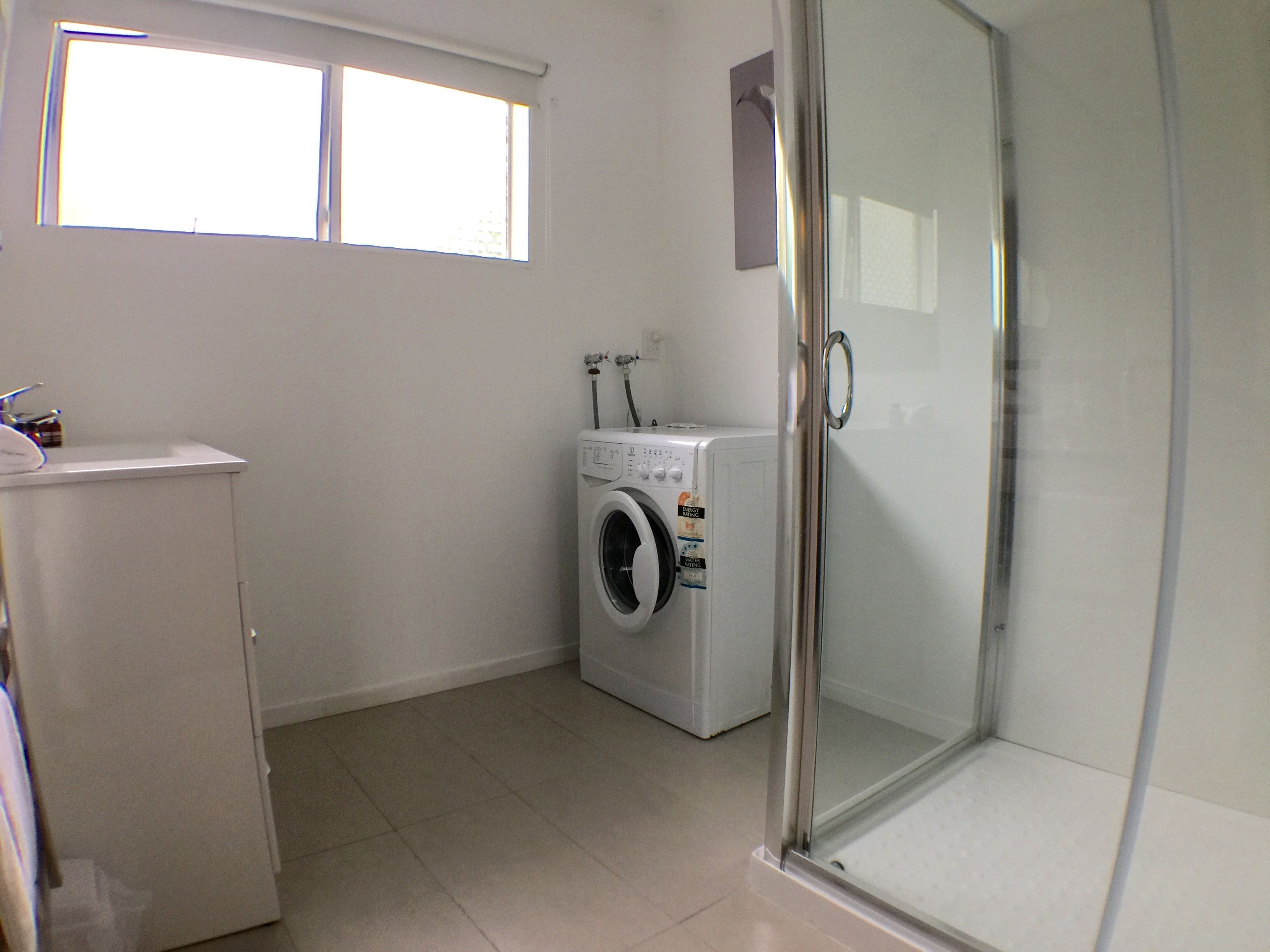 A laundry room with a washing machine, a dryer, and a glass shower enclosure.