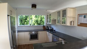 A modern kitchen with white cabinets, a built-in oven, a stainless steel refrigerator, and a window providing a view of greenery outside. - Sea Vista Apartments (Auckland)