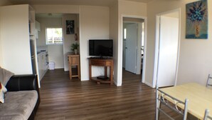 A spacious living area with a wooden floor, a sofa, a TV on a wooden stand, and a dining table with chairs. - Sea Vista Apartments (Auckland)