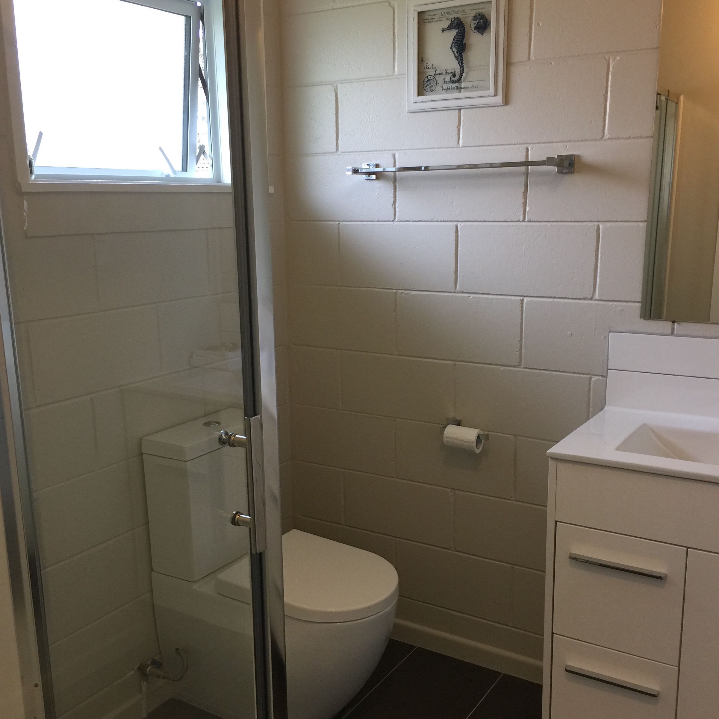 A bathroom with a toilet, a glass shower enclosure, a towel rack, and a framed seahorse picture on the wall.