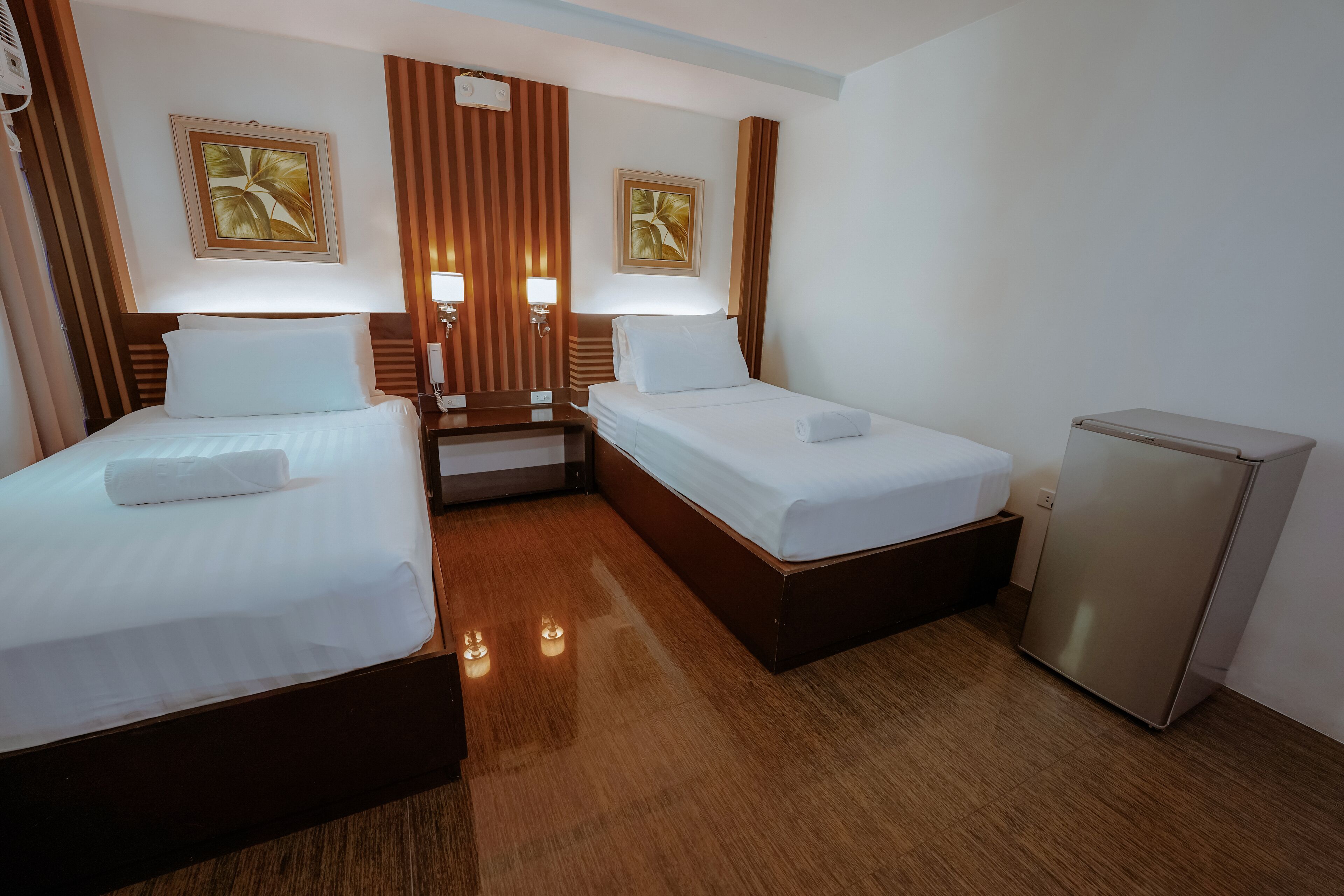 Habitación de hotel con dos camas, un refrigerador pequeño y una mesita de noche con lámpara.