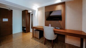 A hotel room with a wooden desk, a television mounted on the wall, a small refrigerator, and a chair. - Emerald Boutique Hotel (Legazpi)