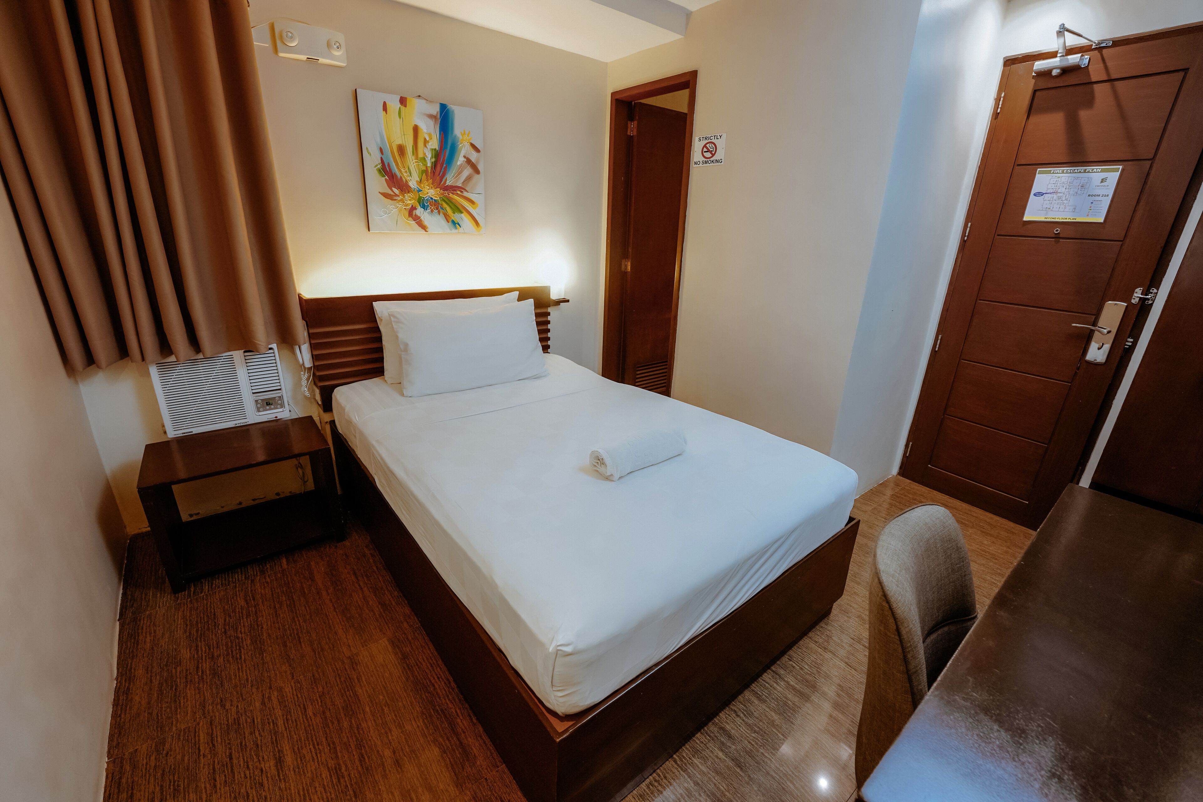 Habitación de hotel con cama, mesita de noche, una silla, puerta de madera y un cuadro en la pared.