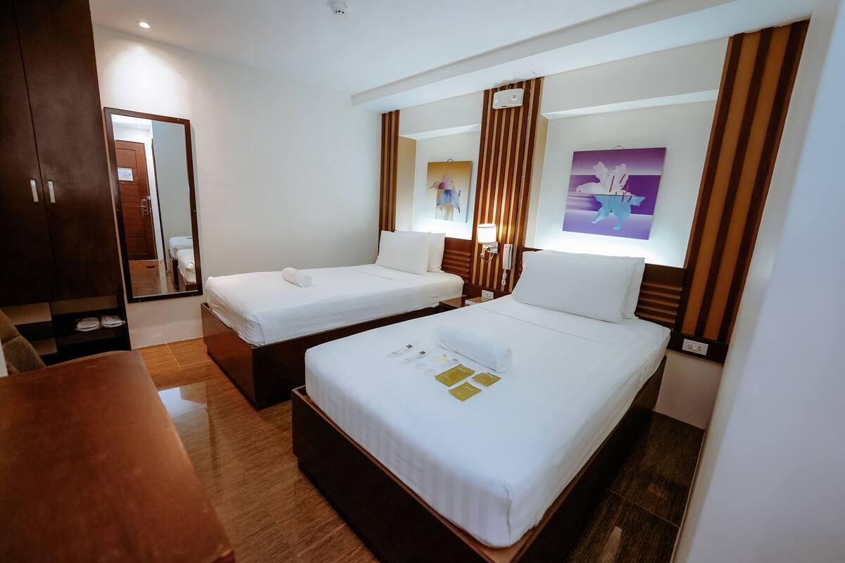 A hotel room with two beds, a wooden wardrobe, a mirror, and a painting on the wall.