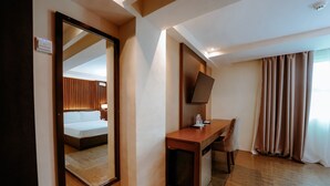 A hotel room with a bed, a desk, a chair, a television, and a window with curtains. - Emerald Boutique Hotel (Legazpi)