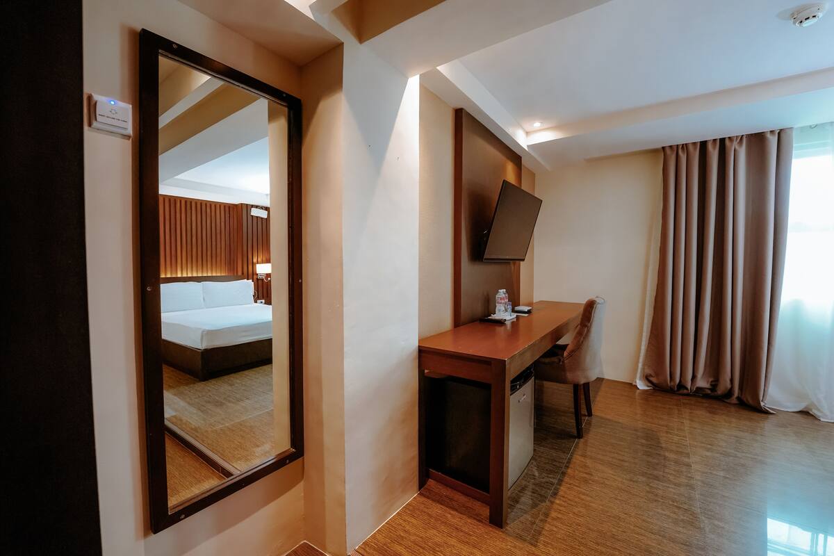 A hotel room with a bed, a desk, a chair, a television, and a window with curtains.