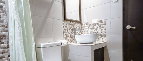 A modern bathroom with a toilet, a sink with a vessel basin, a shower with a glass door, and a dark door.