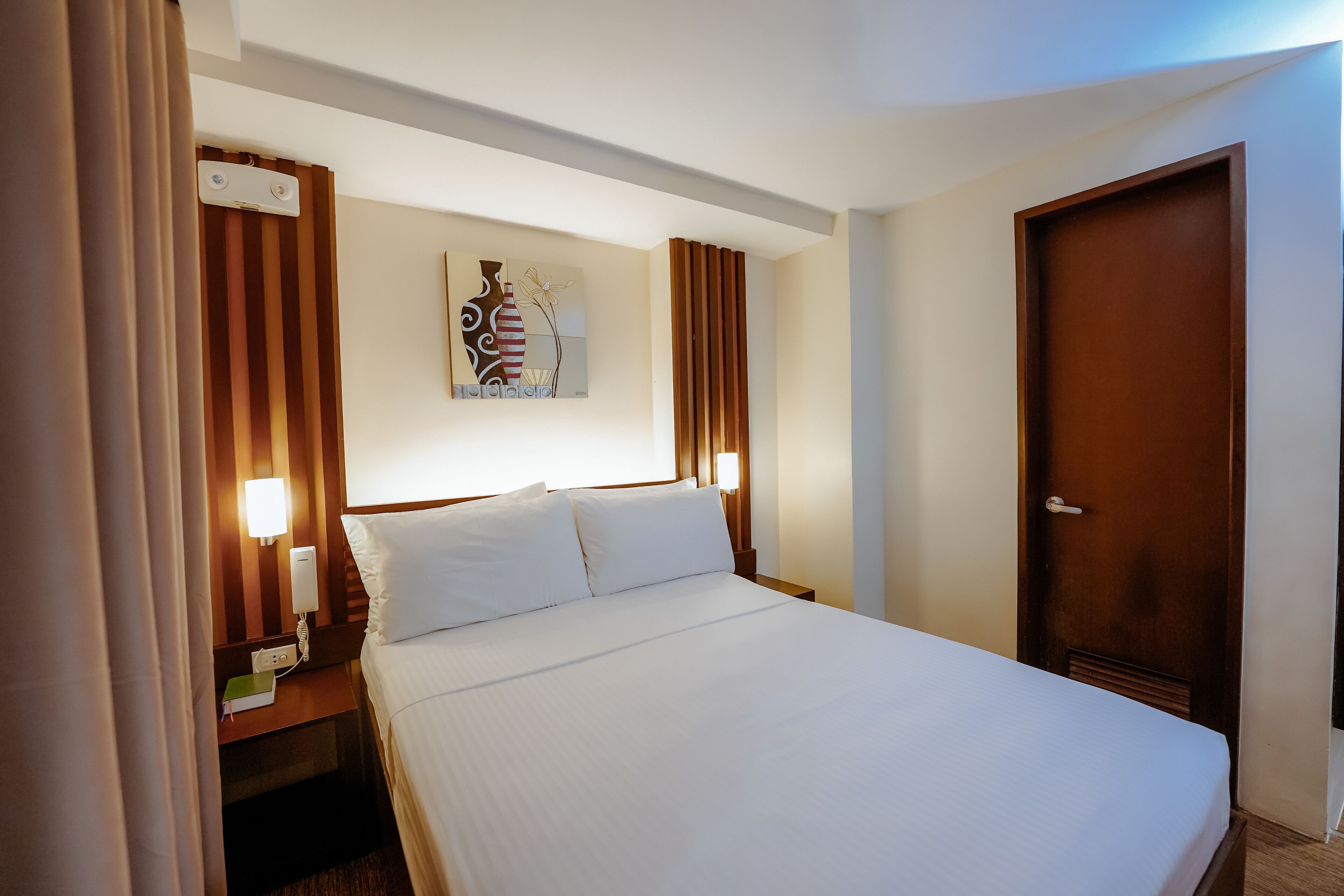 A hotel room with a neatly made bed, a bedside table with a lamp, and a door.