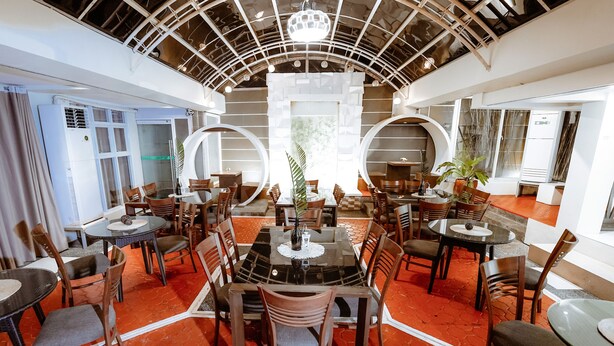 A modern dining area with round tables and chairs, a central decorative plant, and a unique ceiling design. - Emerald Boutique Hotel (Legazpi)