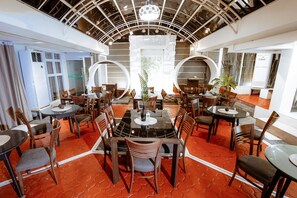 A modern dining area with round tables and chairs, a central decorative plant, and a unique ceiling design. - Emerald Boutique Hotel (Legazpi)