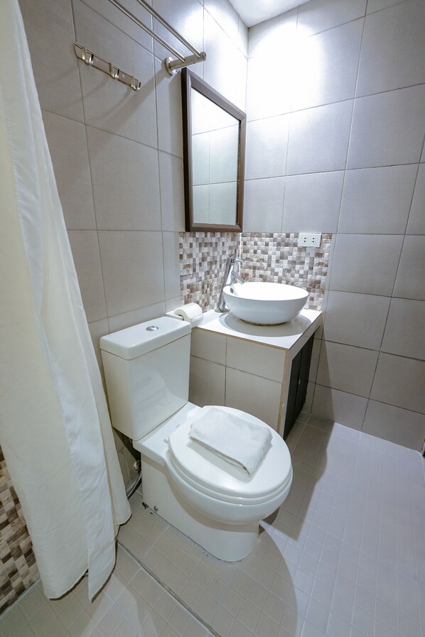 A bathroom with a toilet, sink, and shower curtain. - Emerald Boutique Hotel (Legazpi)