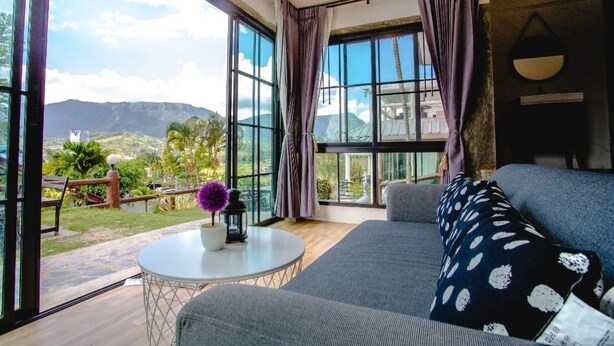 A modern living room with large windows, a round table, and a sofa with patterned cushions.