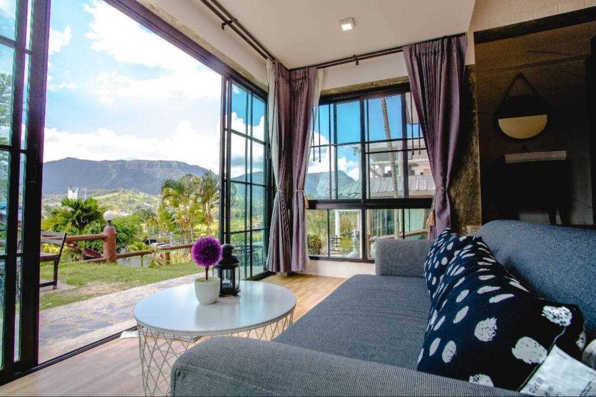 A modern living room with large windows, a round table, and a sofa with patterned cushions.