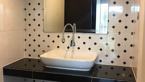 A bathroom with a black countertop, a white sink, and a mirror above it. The walls are tiled with a black and white diamond pattern.