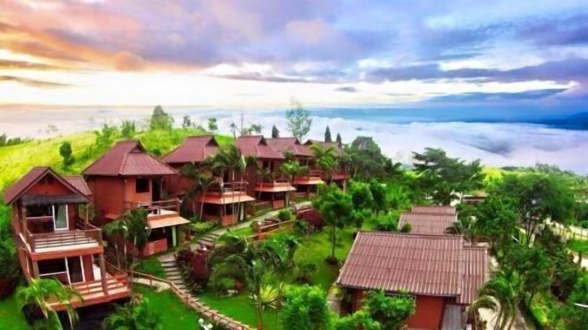 A resort with multiple wooden buildings, some with balconies, surrounded by lush greenery and overlooking a body of water.