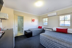 Ein kompaktes Hotelzimmer mit zwei Einzelbetten, einer Küchenzeile, einer Duschkabine und einer kleinen Sitzecke.