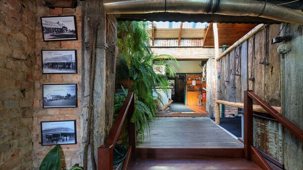 A wooden staircase leading to a covered area with a rustic brick wall and framed historical photos.