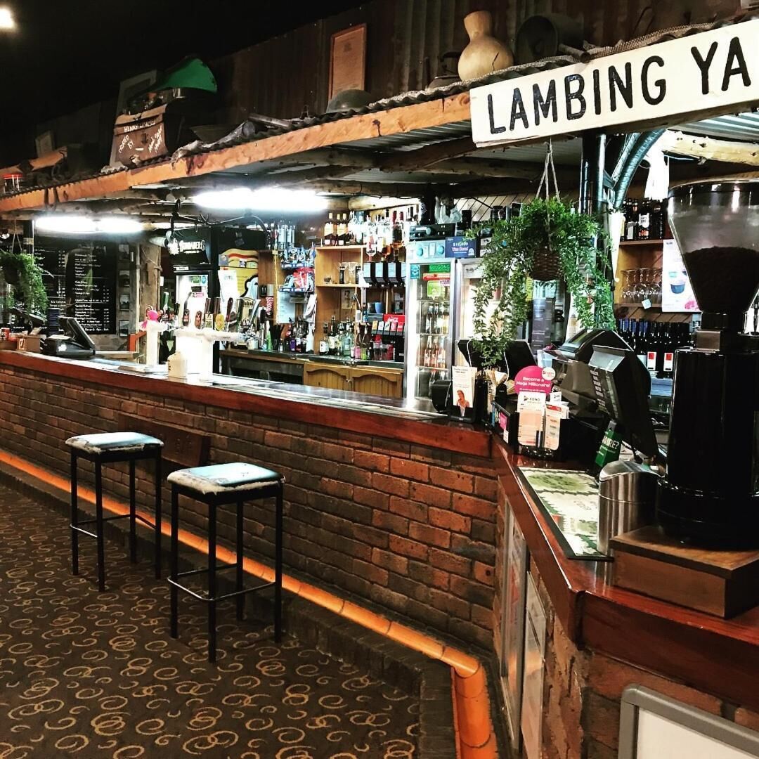 Uma área de bar com banquetas, um letreiro com a inscrição "LAMBING YA" e diversos frascos e equipamentos.