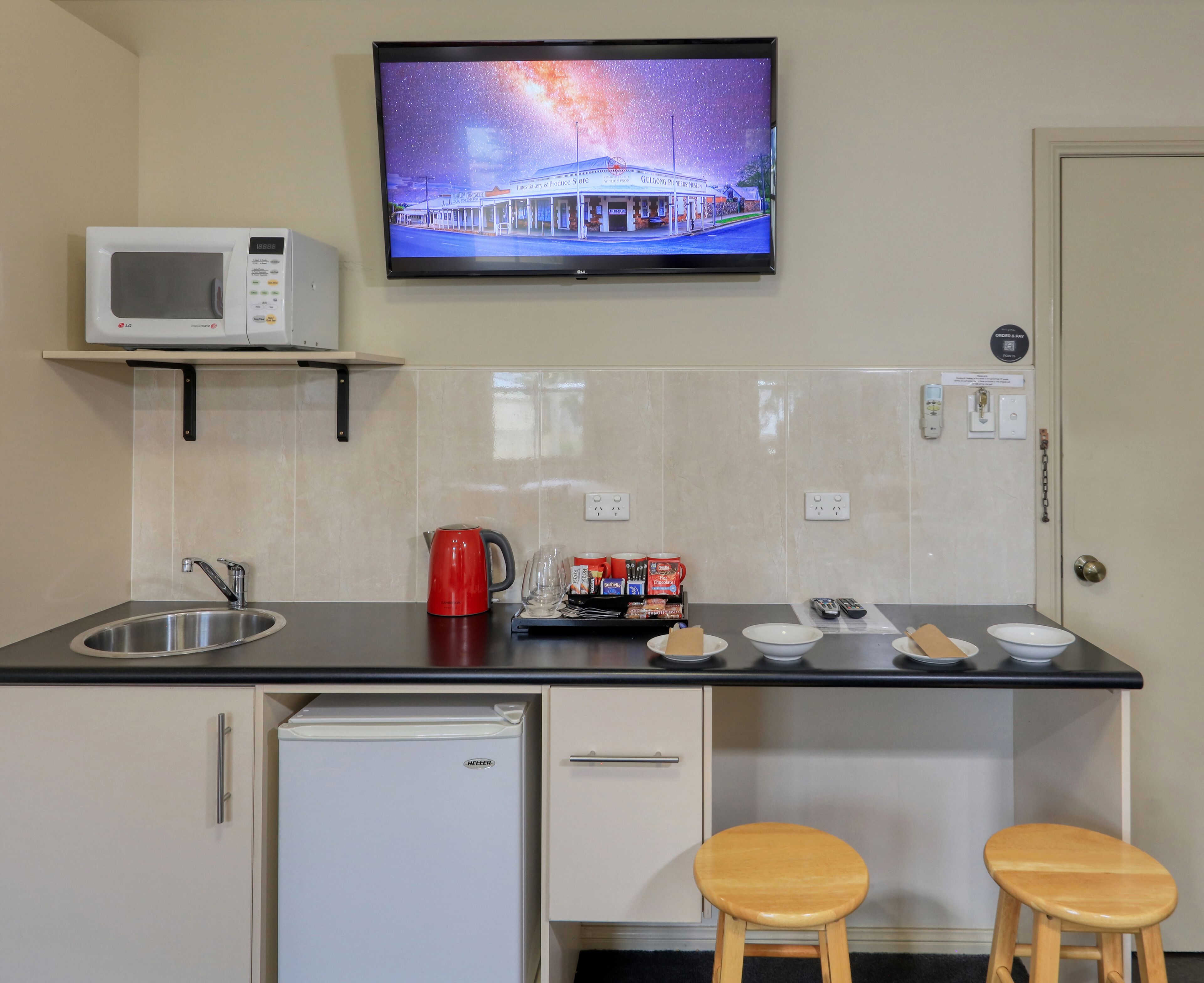 A compact kitchen with a microwave, a coffee maker, and a refrigerator. There are two stools and a sink.