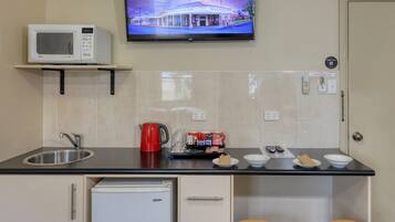 A compact kitchen with a microwave, a coffee maker, and a refrigerator. There are two stools and a sink.