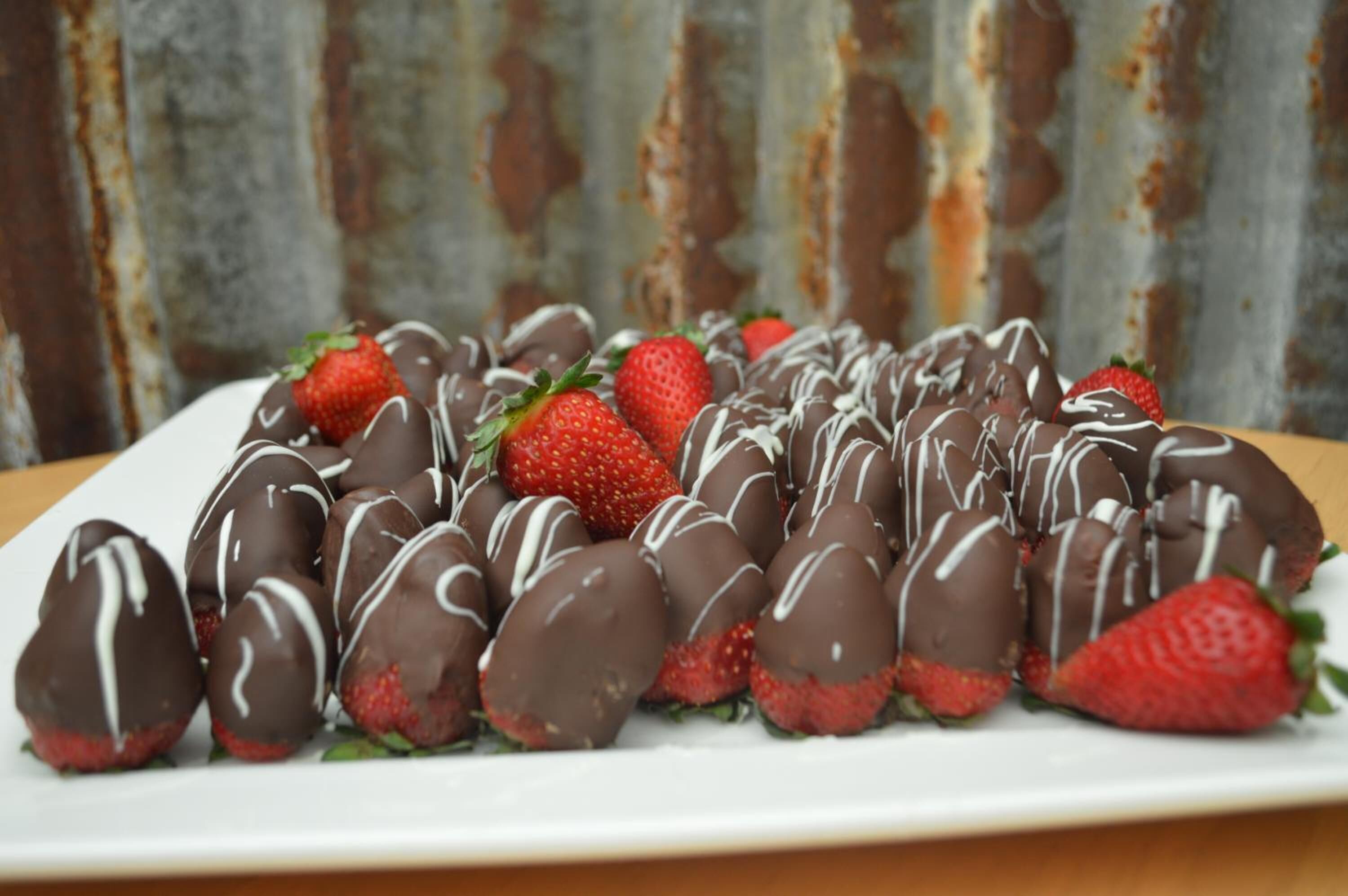 Une assiette de fraises enrobées de chocolat, décorées d’un glaçage blanc, posée sur une assiette blanche.