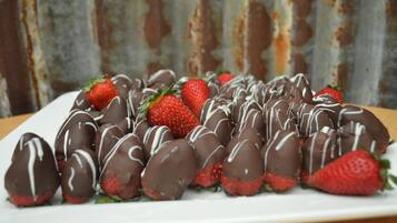 Une assiette de fraises enrobées de chocolat, décorées d’un glaçage blanc, posée sur une assiette blanche.