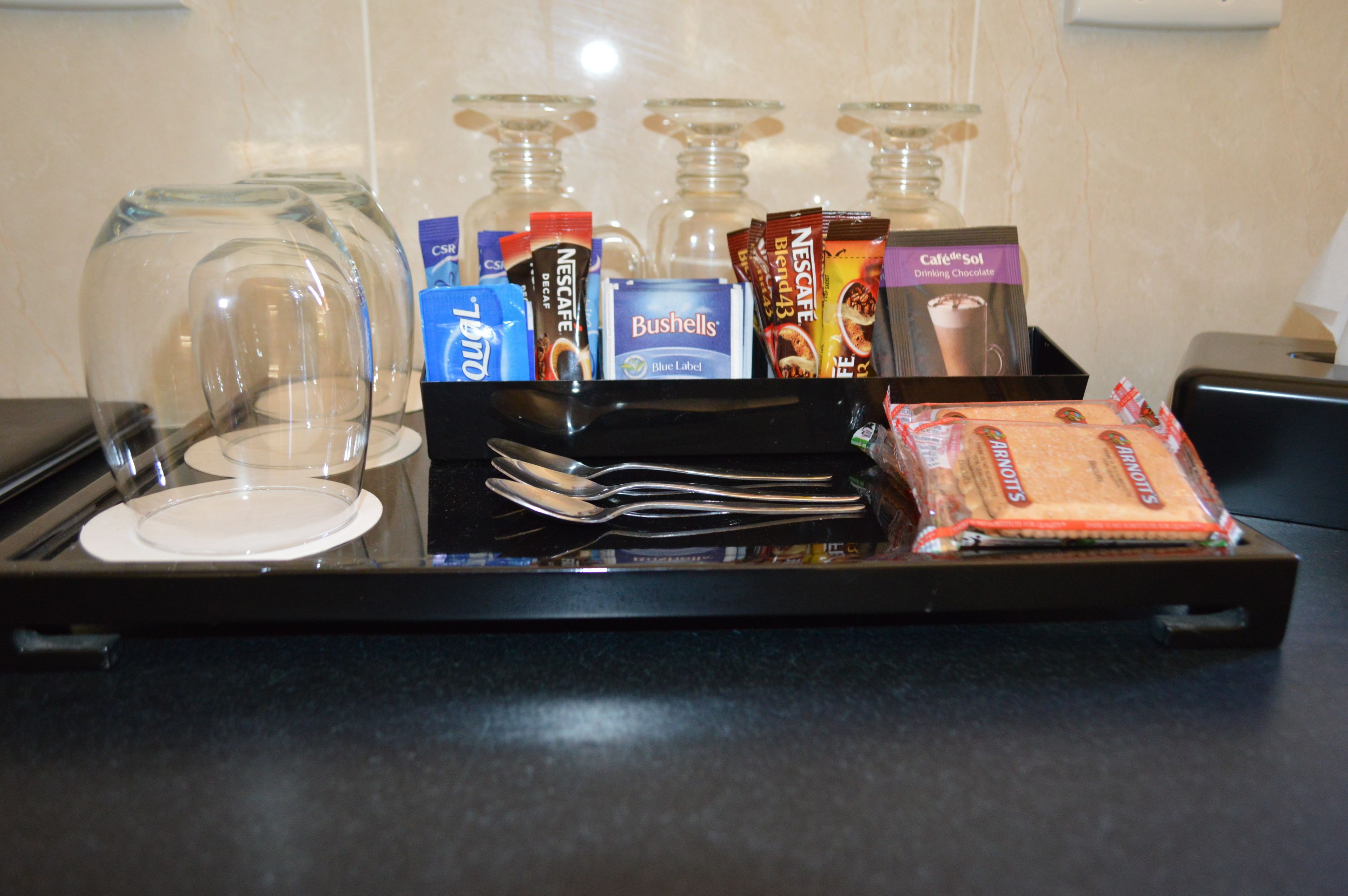 A tray with a coffee maker, a glass carafe, a box of coffee pods, a pack of Nescafe coffee, a pack of Bushells, a pack of Nescafe Blend, a pack of Nescafe Blend 43, a pack of Nescafe Blend 43 with a chocolate flavor, a pack of Nescafe Blend 43 with a caramel flavor, a pack of Nescafe Blend 43 with a hazelnut flavor, a pack of Nescafe Blend 43 with a coffee flavor, a pack of Nescafe Blend 43 with a mocha flavor, a pack of Nescafe Blend 43 with a cappuccino flavor, a pack of Nescafe Blend 43 with a latte flavor, a pack of Nescafe Blend 43 with a cappuccino flavor, a pack of Nescafe Blend 43 with a latte flavor, a pack of Nescafe Blend 43 with a cappuccino flavor, a