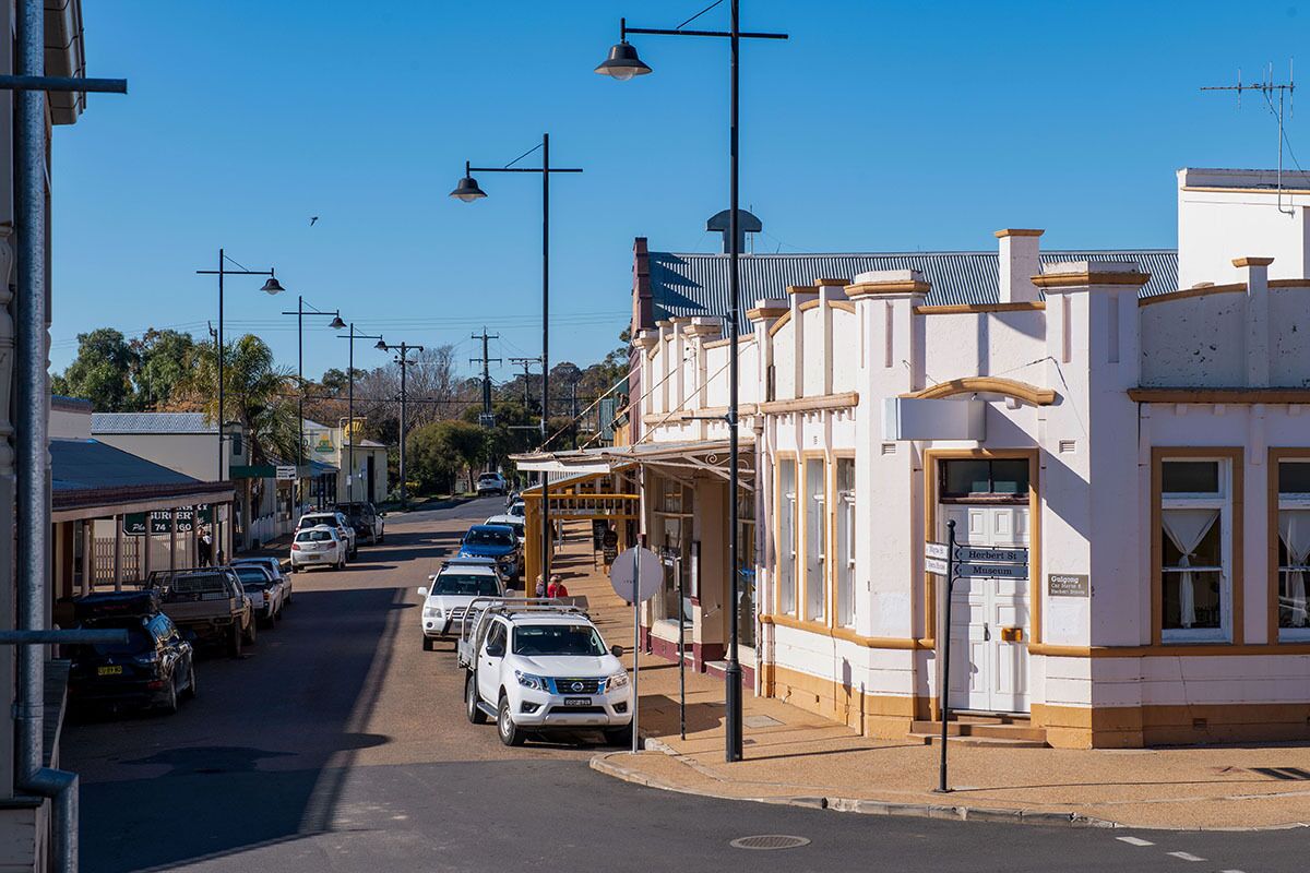 A street view with a row of parked cars, a building with a white facade, and a clear blue sky.