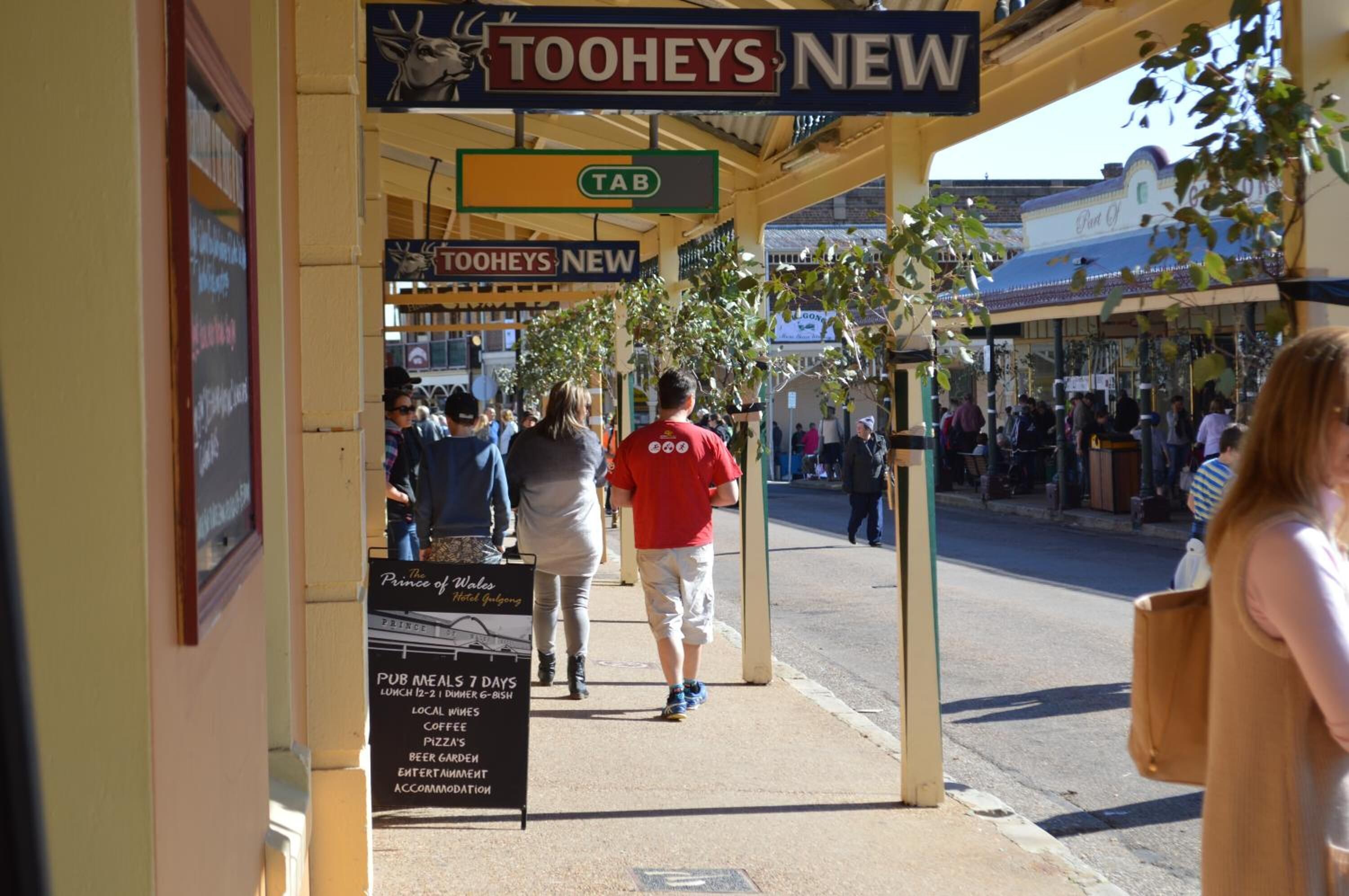A street scene with a sign for 'Tooheys New' and a 'Pub Meals 7 Days' sign.