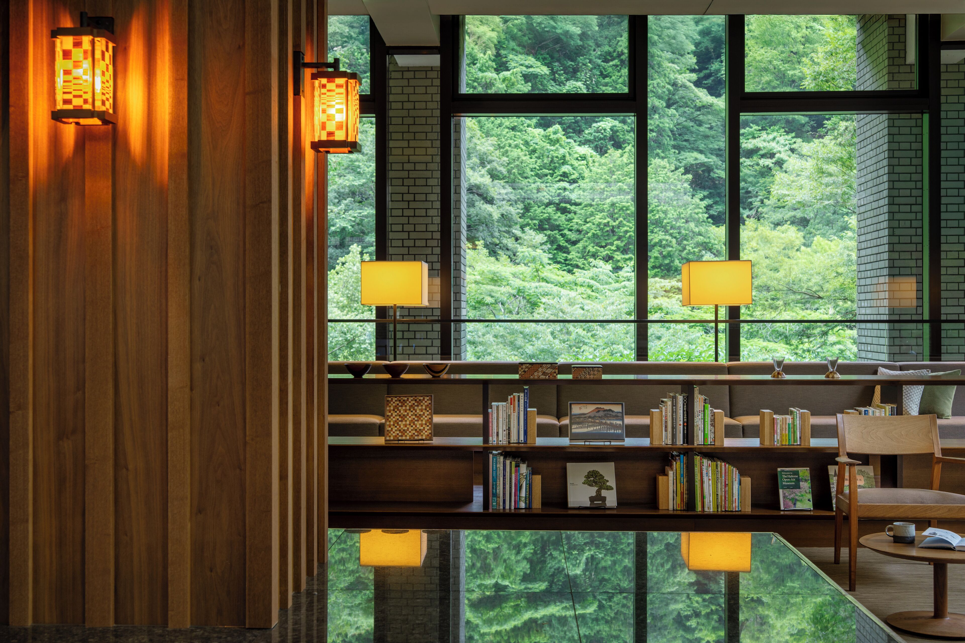 A room with a large window, a bookshelf, and two wall-mounted lamps.