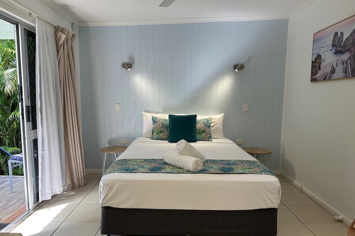A bedroom with a bed, a nightstand, a small table, and a view of the outdoors.