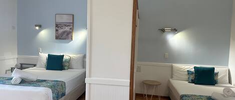 Habitación de hotel con dos camas, un ventilador de techo, una pequeña mesa redonda y un cuadro en la pared.