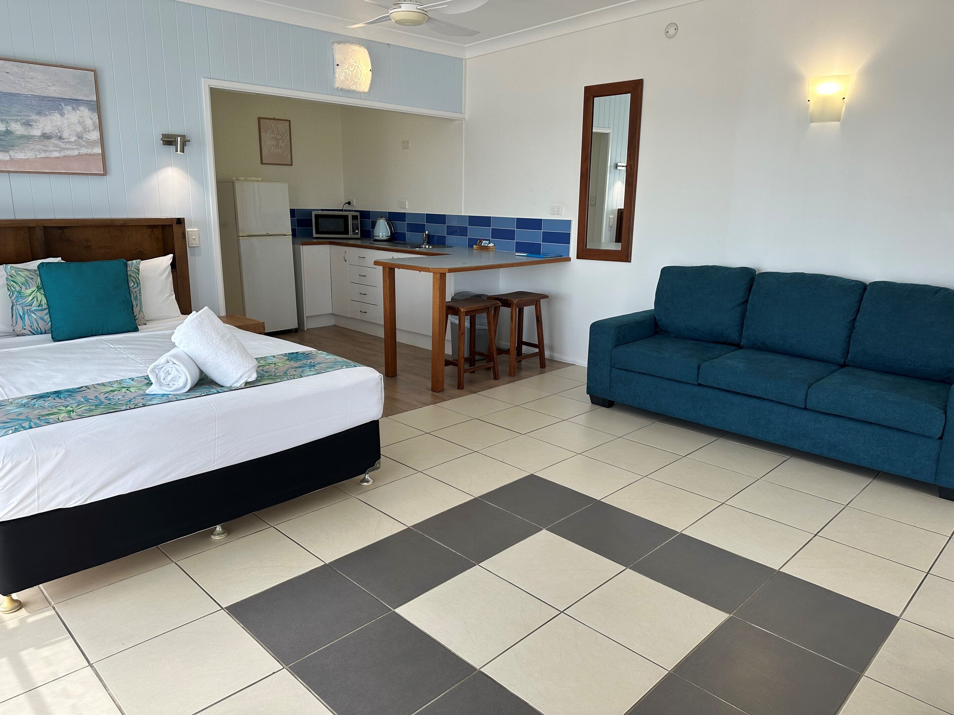 Een hotelkamer met een bed, een blauwe bank, een kitchenette en een eethoek.