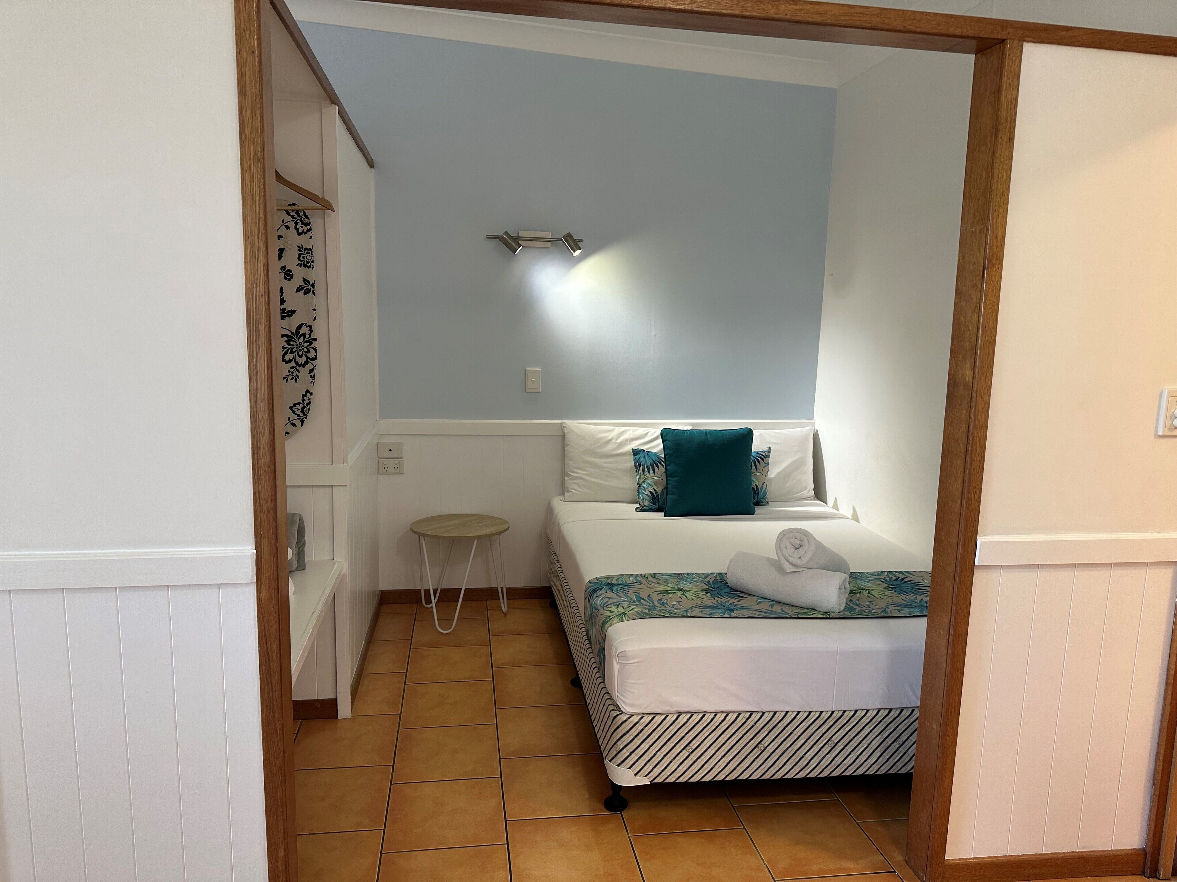 A small, neatly arranged bedroom with a bed, a small stool, and a nightstand.